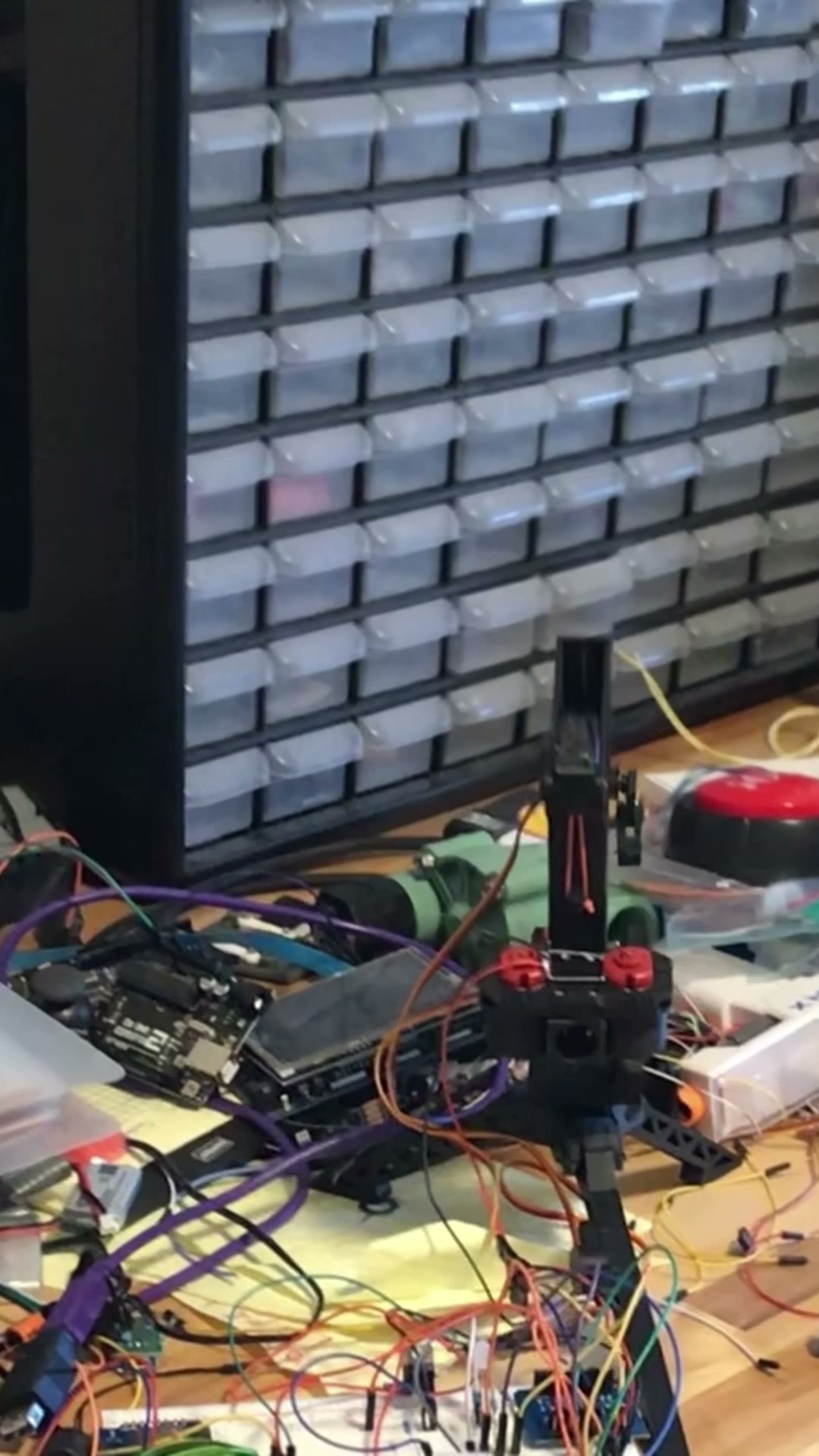 Motorized turret mechanism on a workbench, with a camera, wiring, and a red button